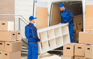 Young Male Movers Unloading Furniture And Cardboard Boxes From Truck On Street