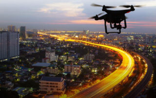 Silhouette Of Drone Flying Above City At Sunset