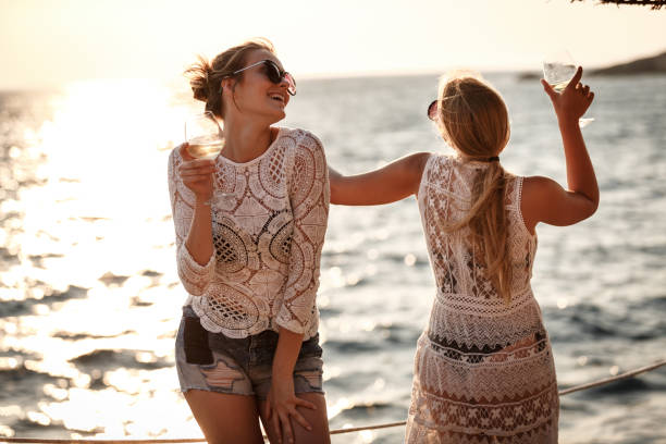 Two Young Women Are Dancing And Having Wine At The Beach.